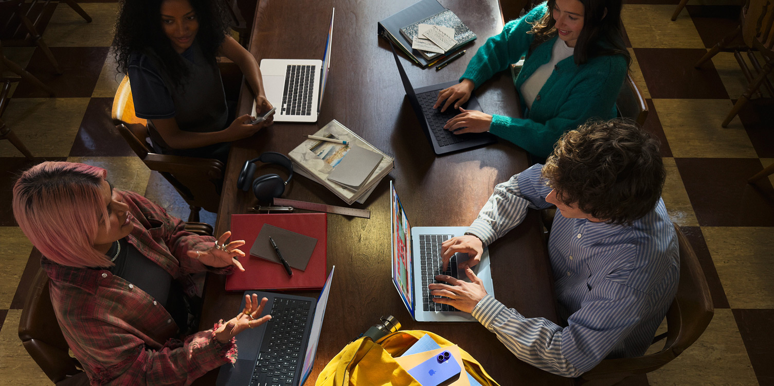 Quatre personnes assises autour d’une table pour étudier, avec leurs MacBook ouverts et leurs notes à portée.