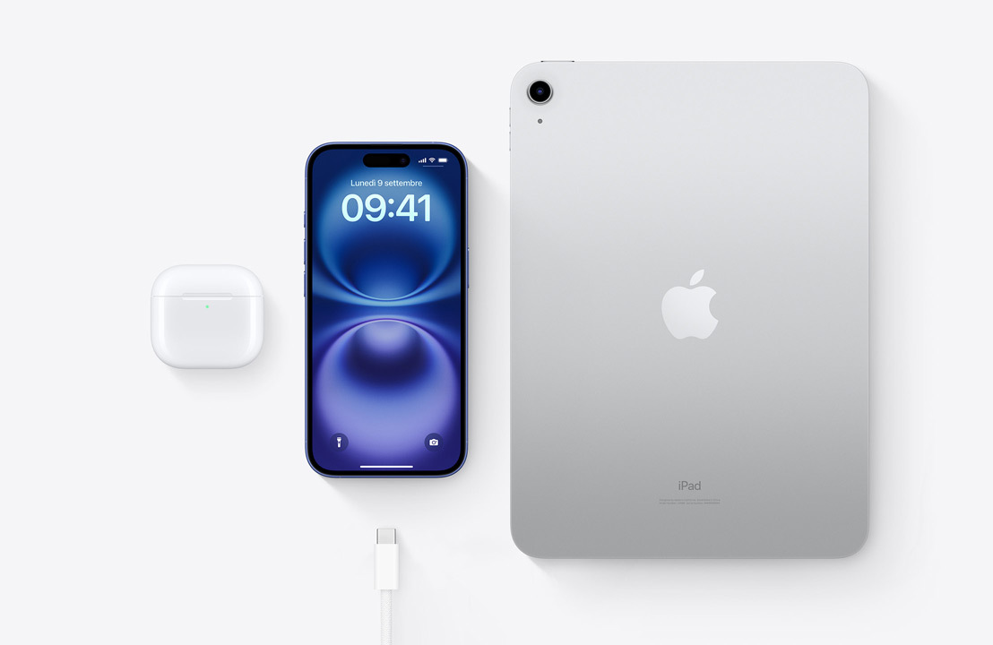 Un paio di AirPods Pro nella custodia di ricarica, un iPhone 16, un iPad e un cavo con connettore USB-C, per mostrare che tutti e tre i dispositivi si possono caricare con lo stesso cavo USB-C