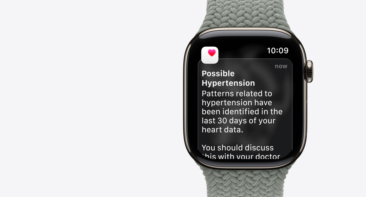 Apple Watch Series 11, kleur goud, kast van titanium, melding bij mogelijke hoge bloeddruk, roze hart in wit vlak, rechterkant, Digital Crown, bandje, groengrijs gevlochten solobandje