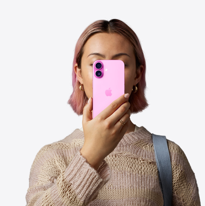 Una persona sostiene un iPhone 16 rosa frente a su rostro y se ve la parte posterior, con el sistema de dos cámaras en la esquina superior izquierda.