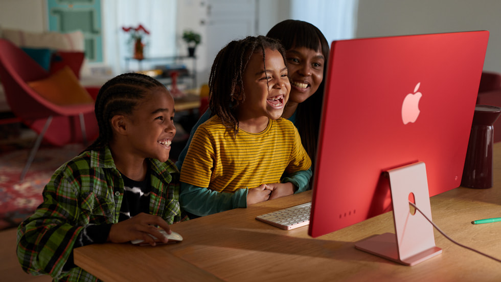 İki çocuk ve bir ebeveyn, M3 çipe sahip pembe renkli yeni iMac ve uyumlu renkte klavye ile fareyi kullanırken gösteriliyor.