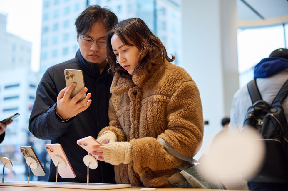 iPhone 15 제품들을 살펴보고 있는 두 명의 고객.