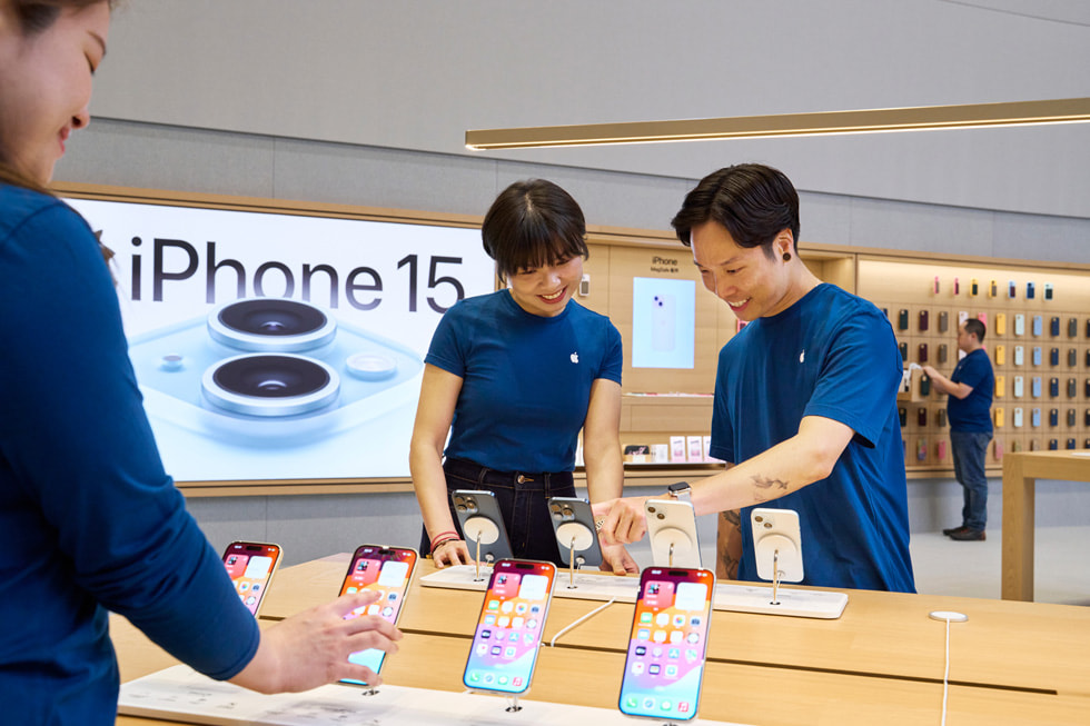 Team members look at iPhone 15 devices on a display table in the store.