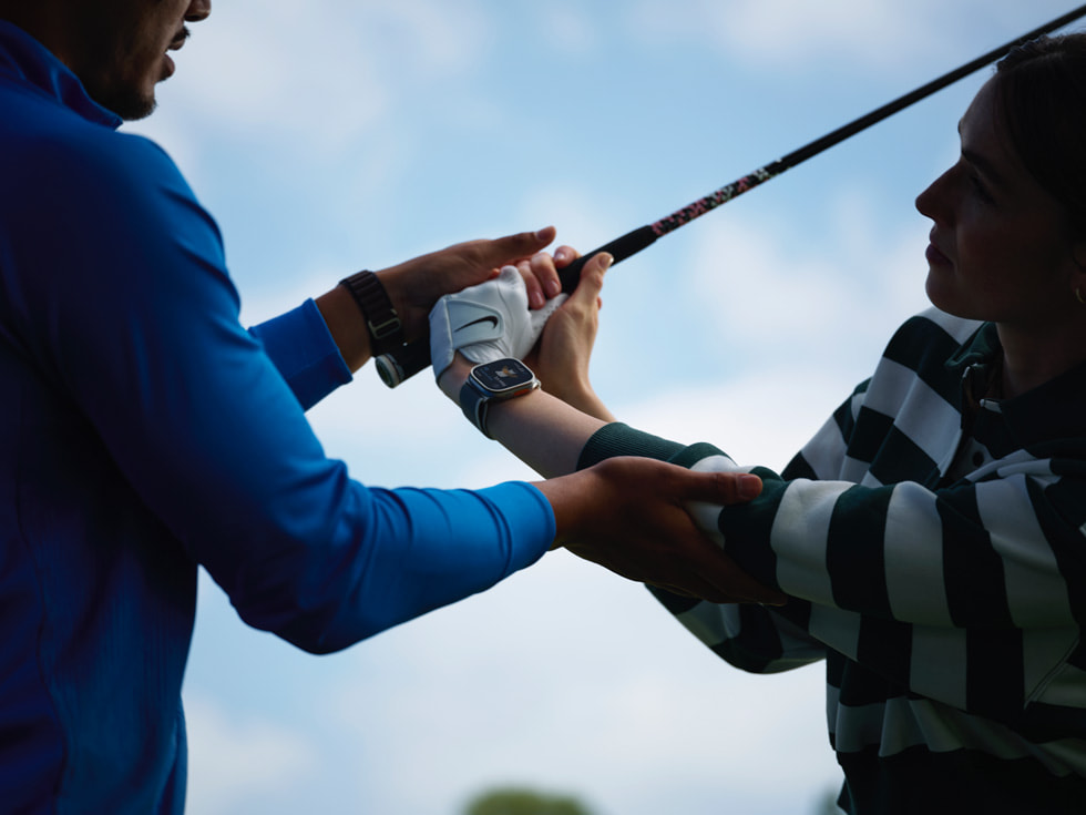 Bilde av en golfinstruktør som hjelper en golfer med svingen, og golferen har på seg en Apple Watch.
