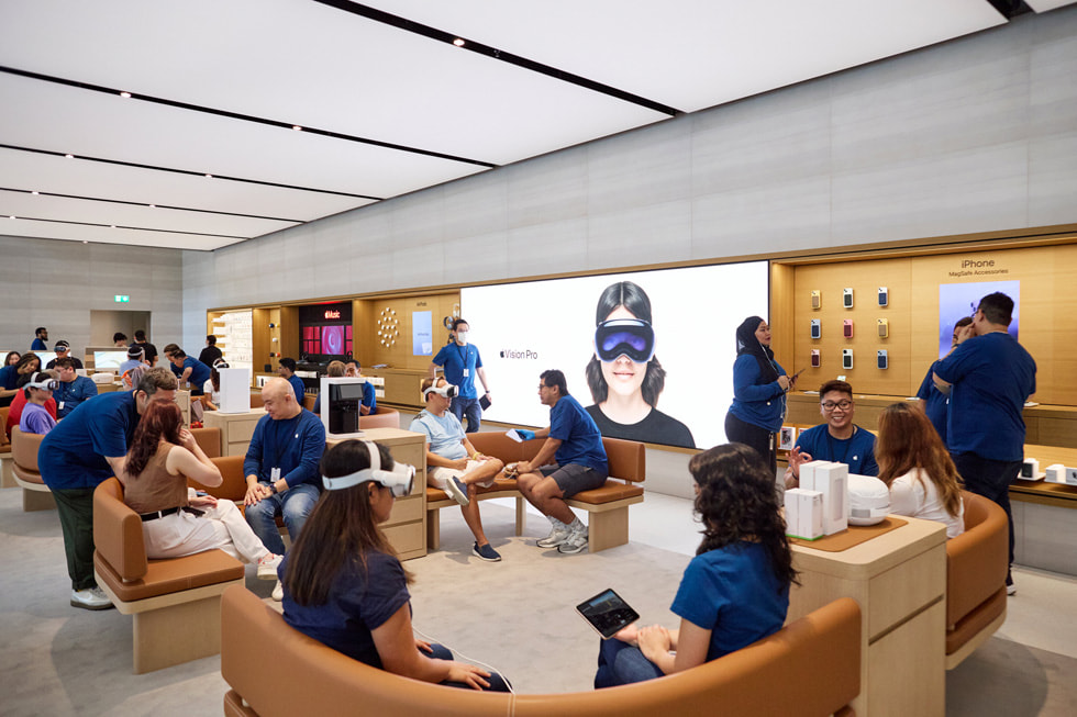 Una imagen panorámica de la zona de prueba dentro de la tienda Apple Orchard Road, con clientes e integrantes del equipo sentados en bancos curvos.
