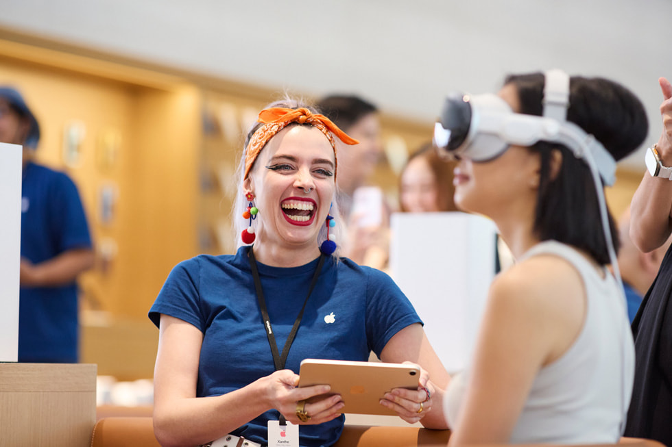 Una integrante del equipo con una gran sonrisa y un cliente probando el Apple Vision Pro.