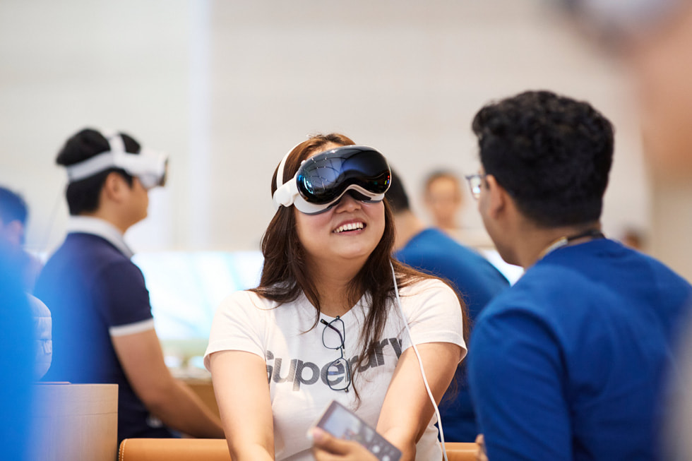 Una clienta con un Apple Vision Pro sonríe mientras habla con un integrante del equipo que está junto a ella.