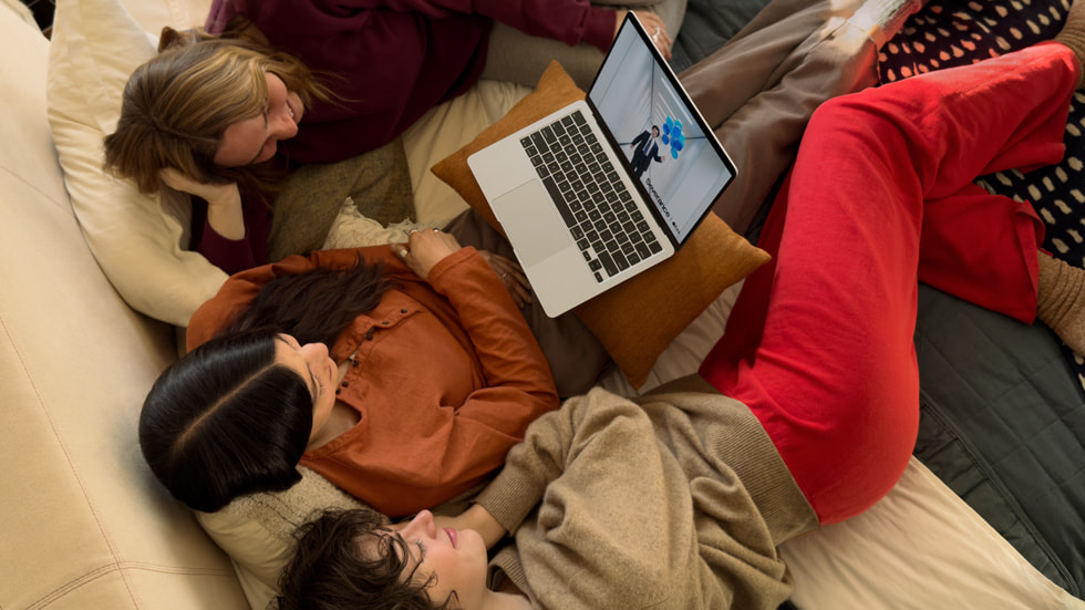 Trzy osoby siedzące na kanapie oglądają serial Rozdzielenie na MacBooku Air.
