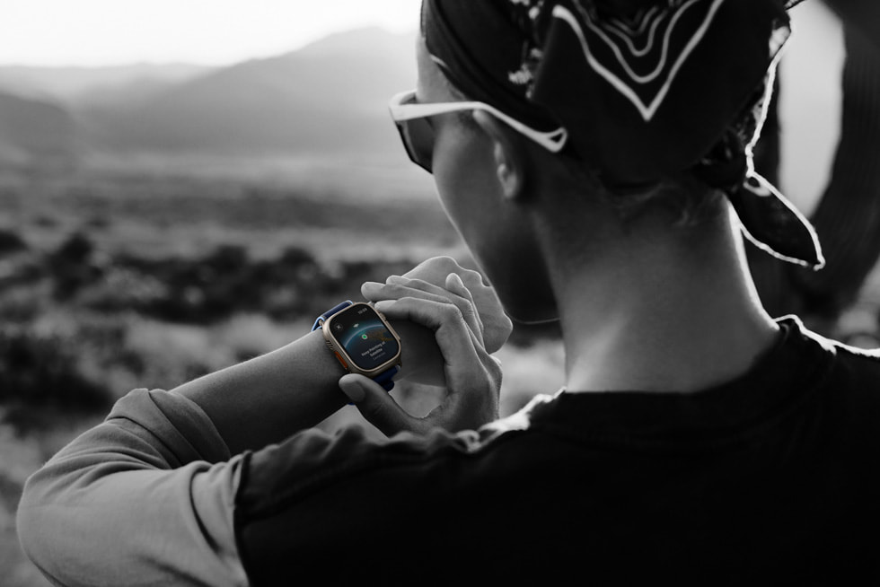 A black-and-white photo of a runner checking their satellite connection on Apple Watch Ultra 3 in a desert landscape.