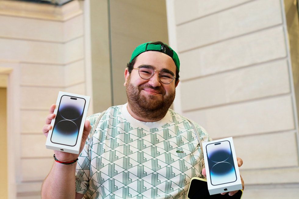 عميل يقف خارج متجر Apple Champs-Élysées ينظر إلى نافذة تعرض أجهزة iPhone متنوعة.