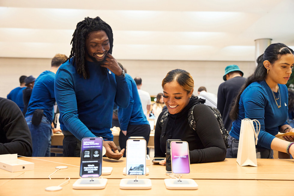 أحد أعضاء فريق متجر Apple Fifth Avenue يساعد عميلة على طاولة عرض جهاز iPhone 14. 