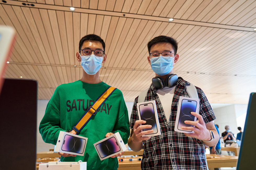 عميلان يمسك كل منهما بجهازي iPhone 14 Pro في متجر Apple Sanlitun.