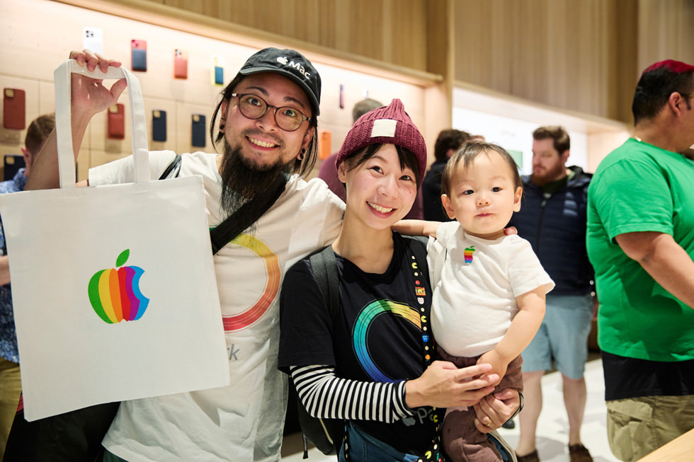 To kunder med Apple-udstyr har en Apple-pose i hånden, mens den ene holder en baby.