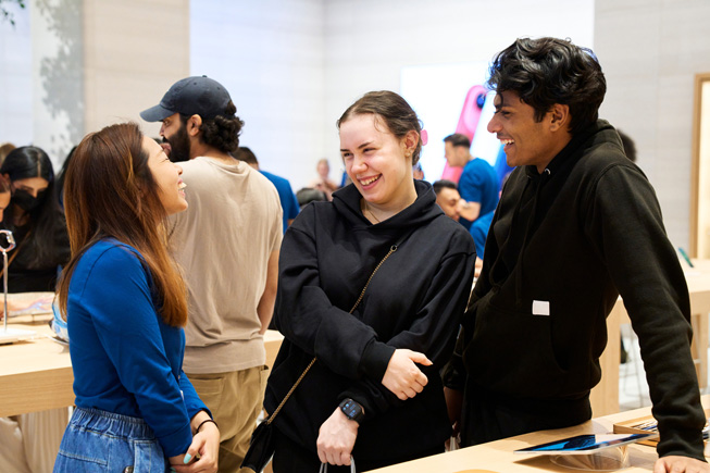 Apple-ansatte og kunder snakker sammen i en Apple Store.