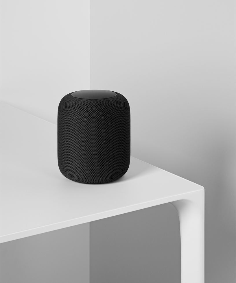 Beyaz masanın üzerinde duran siyah bir HomePod’un fotoğrafı. 