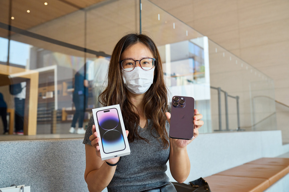 عميلة في متجر Apple Sanlitun تمسك بجهاز iPhone 14 Pro الجديد باللون الليلكي لتلتقط صورة معه.