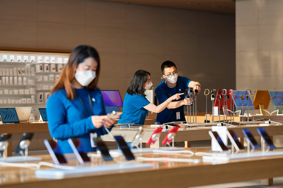 أحد أعضاء فريق متجر Apple Sanlitun ينظر إلى أجهزة iPhone بينما يظهر في الخلفية عضوان آخران يعملان على تعديل عرض لساعة Apple Watch.