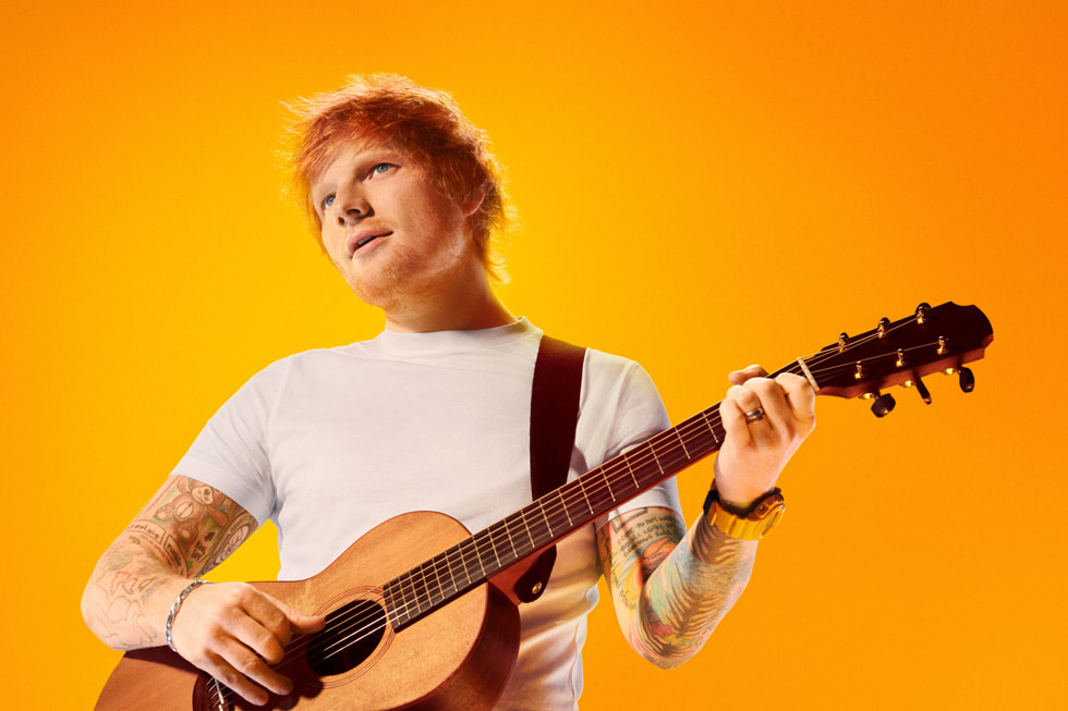Şarkıcı ve şarkı yazarı Ed Sheeran, turuncu bir arka planın önünde gitar çalarken gösteriliyor.