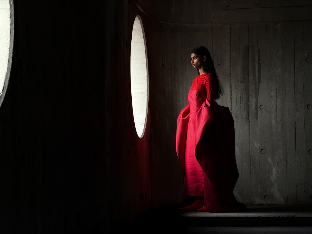 A woman wearing a long red dress stands in an empty room being photographed. The Photo app toggles through the following focal lengths to demonstrate the capabilities of the pro camera system: 200 mm, 100 mm, 48 mm, 35 mm, 28 mm, 13 mm and macro