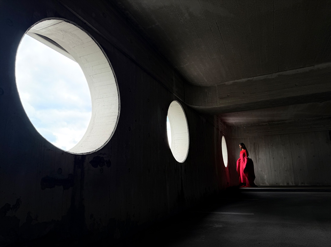 A woman wearing a long red dress stands in an empty room being photographed. The Photo app toggles through the following focal lengths to demonstrate the capabilities of the pro camera system: 200 mm, 100 mm, 48 mm, 35 mm, 28 mm, 13 mm and macro